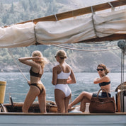 Three women in swimsuits on a boat with a scenic background