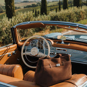Brown leather handbag on the seat of a vintage convertible car with vineyard landscape in the background