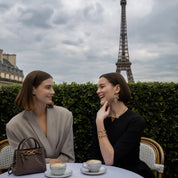 Two women sitting at a table with coffee in front of the Eiffel Tower.