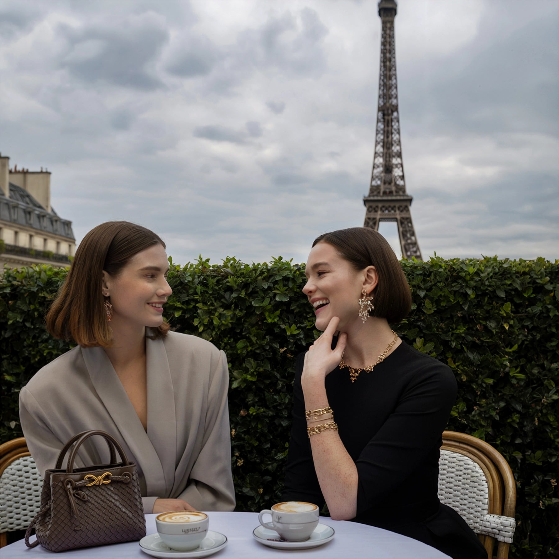 Two women sitting at a table with coffee in front of the Eiffel Tower.