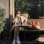 Woman sitting at an outdoor cafe table, drinking a beverage.