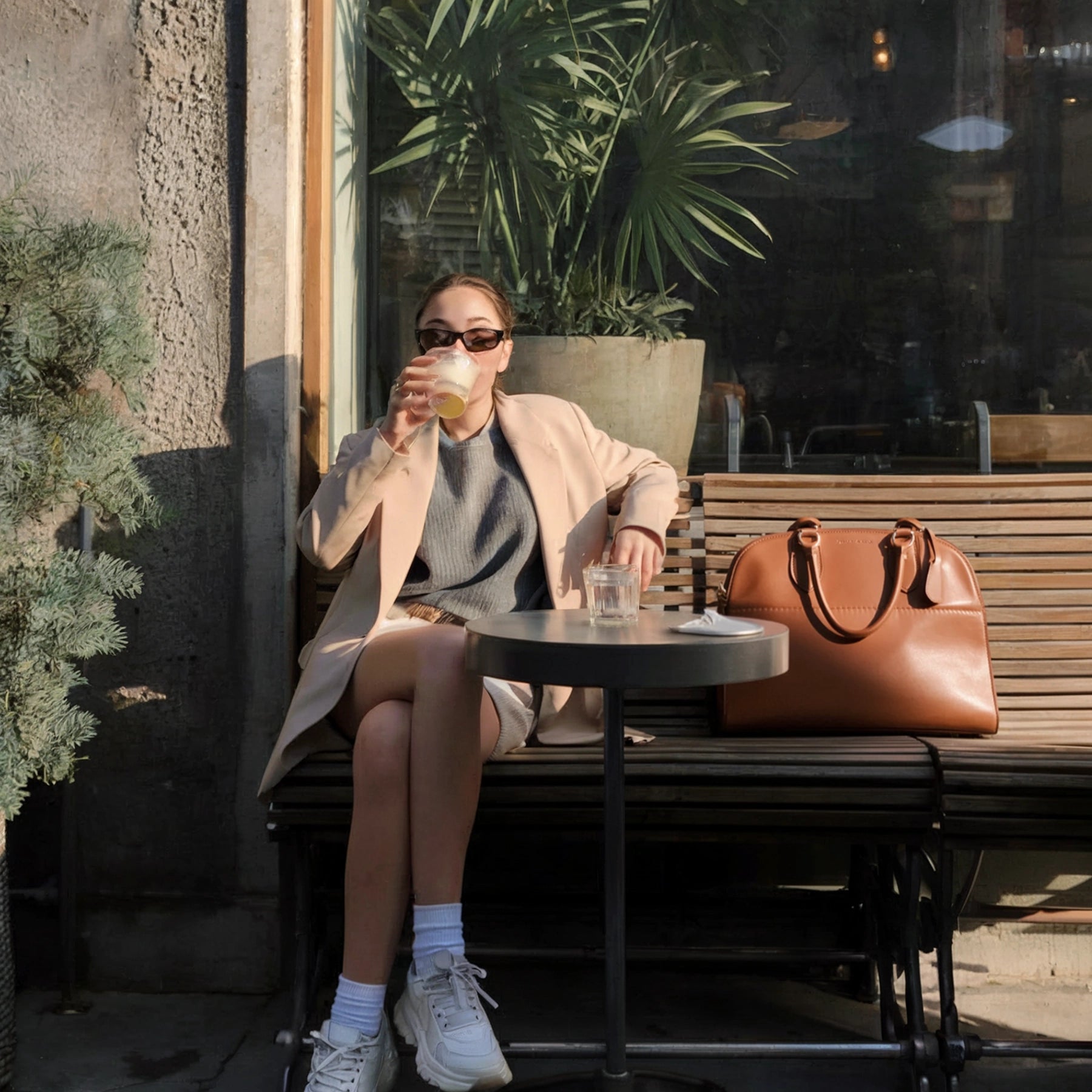 Woman sitting at an outdoor cafe table, drinking a beverage.