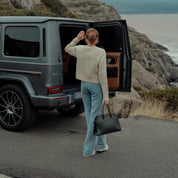 Person opening the door of a gray SUV by a coastal road