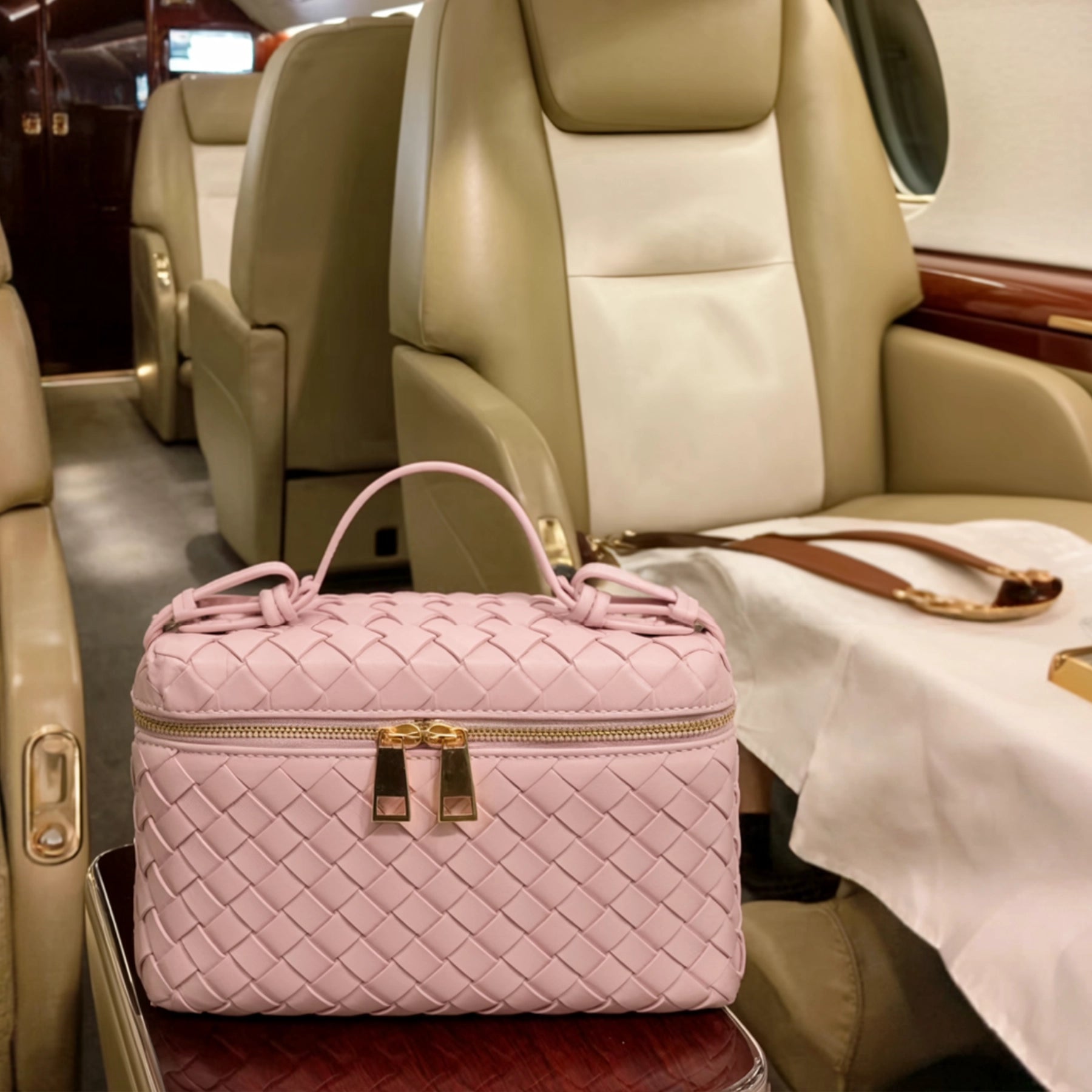 Pink quilted handbag with gold accents on a seat inside a luxury vehicle.