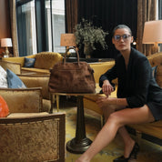 Woman sitting on a couch in a stylish room with a brown handbag.